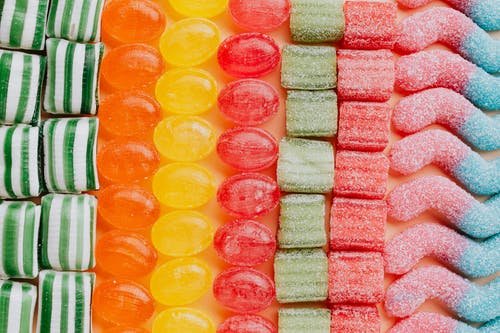 Image of Composition of yummy multicolored candies in rows against peachy background
