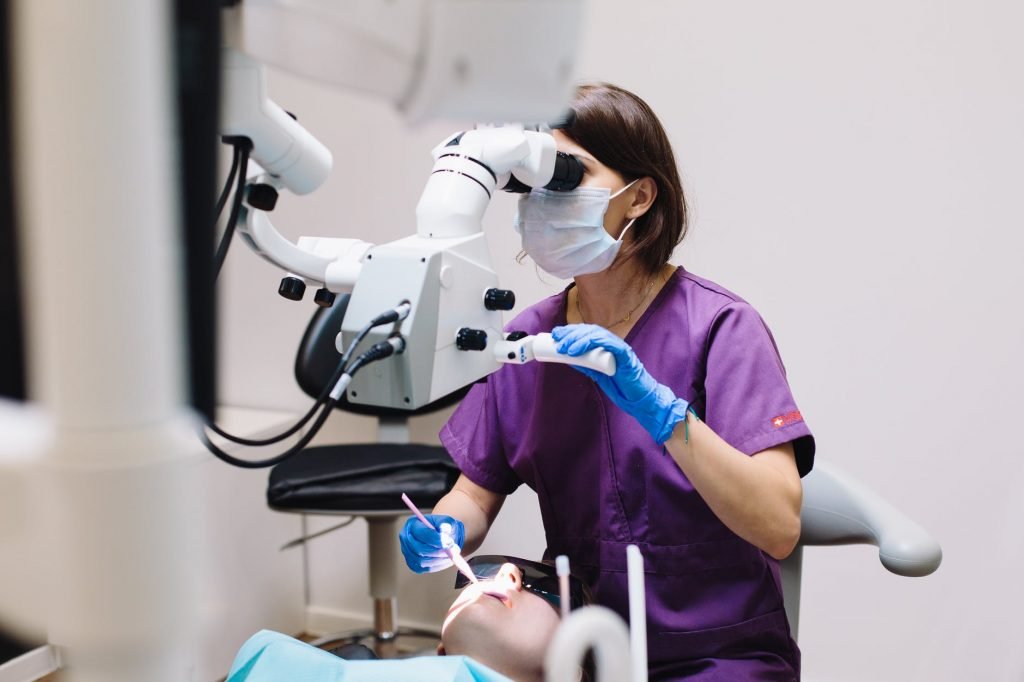Image of Woman in Purple Scrub Using a Dental Equipment in Examining a Patient