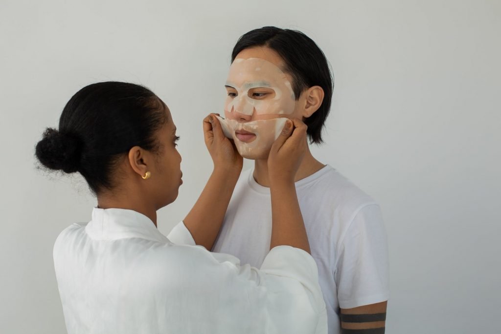 Image of Ethnic beautician applying sheet mask on face of Asian client