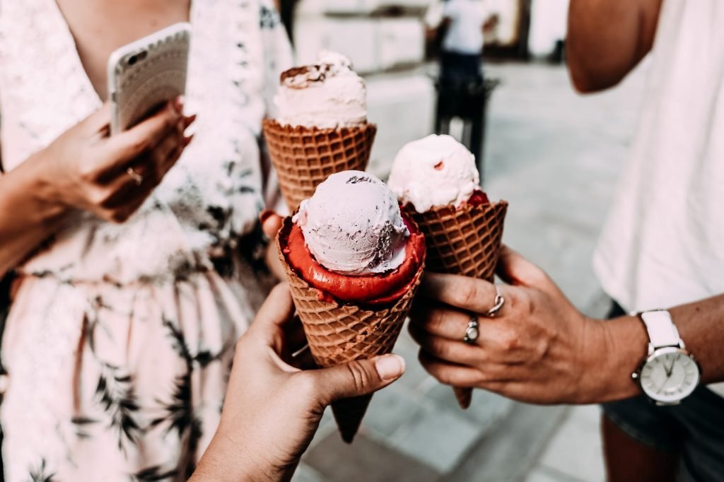 Image of Crop unrecognizable friends clinking ice creams on street