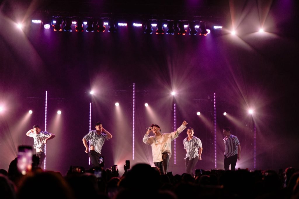 Image of Photo of Man Singing on Stage With Backup Dancers