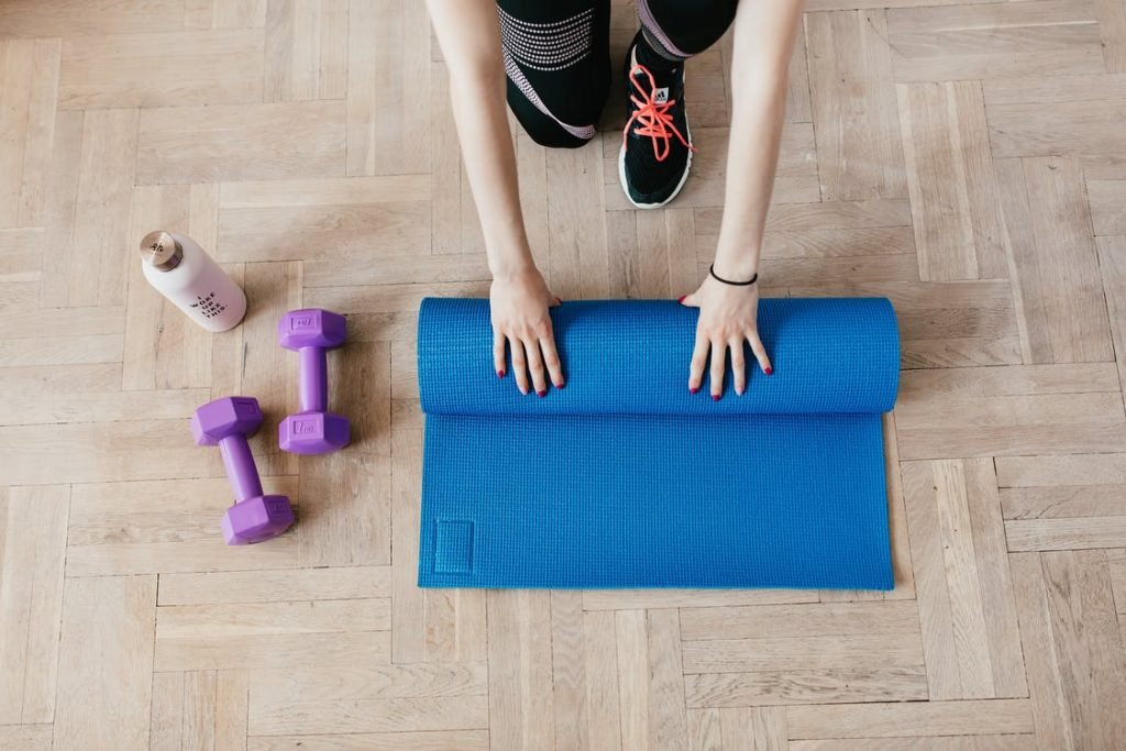 Image of Crop sportswoman unfolding sport mat on wooden floor