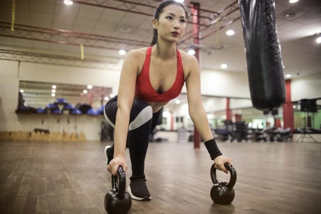 Image of Strong determined ethnic woman stretching body using kettlebells