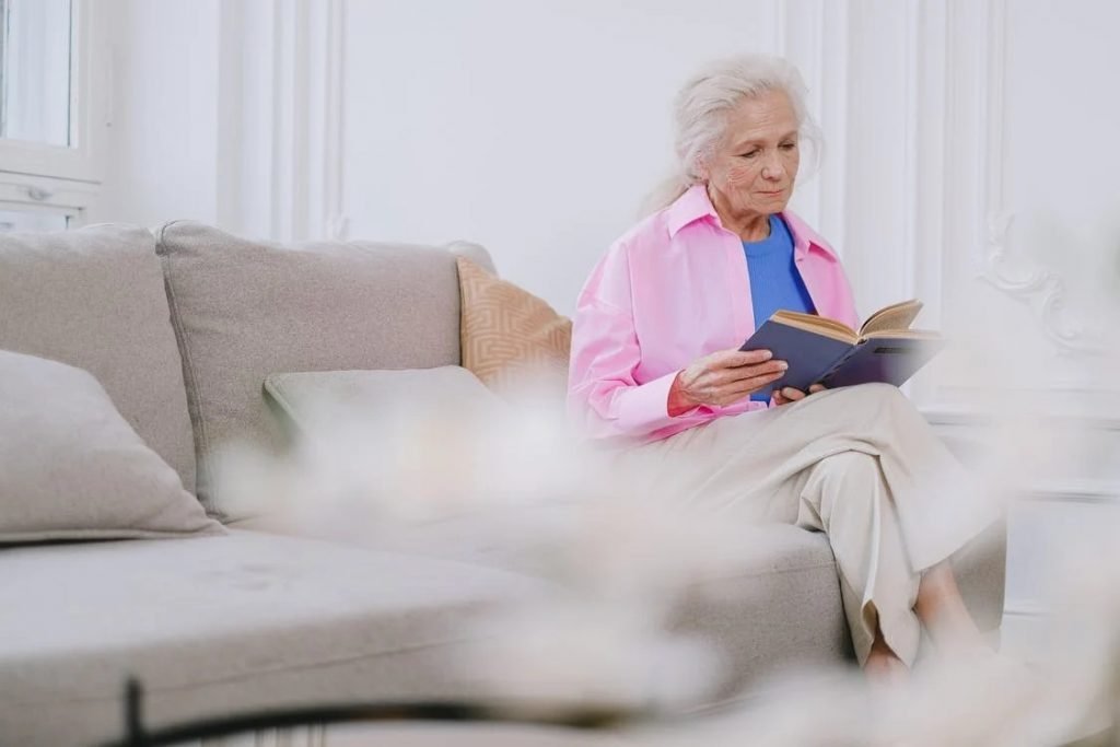Image of Elderly Woman Sitting on a Sofa While Reading a Book