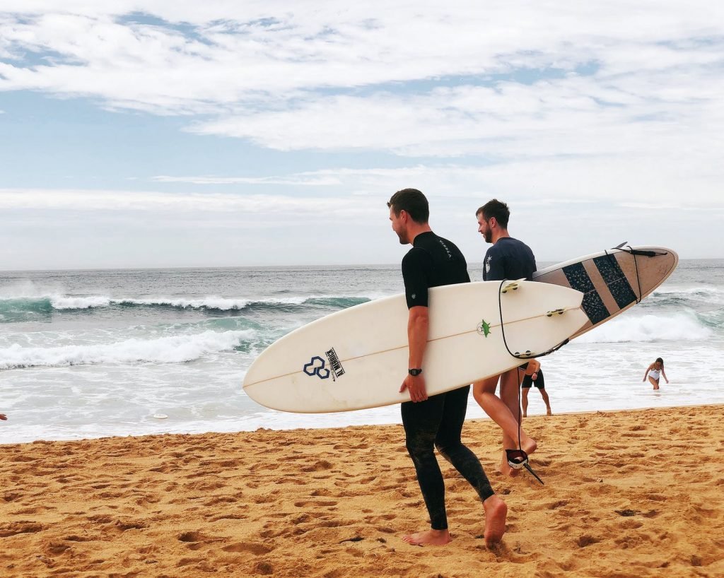 Image of Two Men Carrying Surfboards Near Seashore