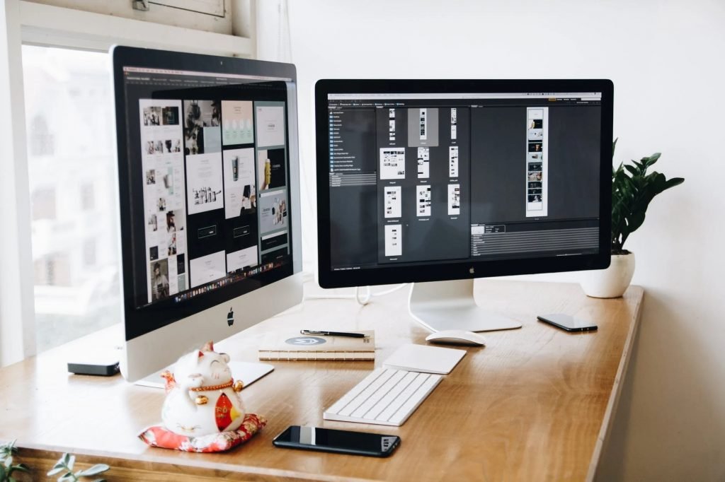 Image of Two Imac's With Keyboard and Phones on Desk