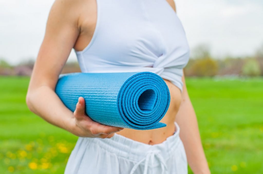 Image of Woman Standing and Holding Blue Yoga Mat